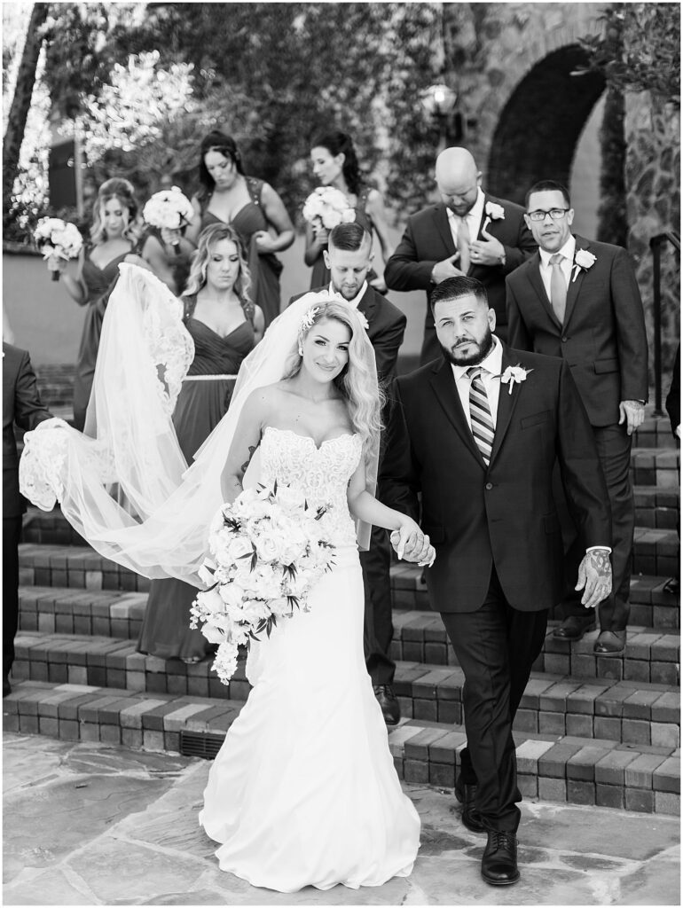 bride and groom walking down staircase with wedding party in black and white photo at Bella Collina Orlando Wedding