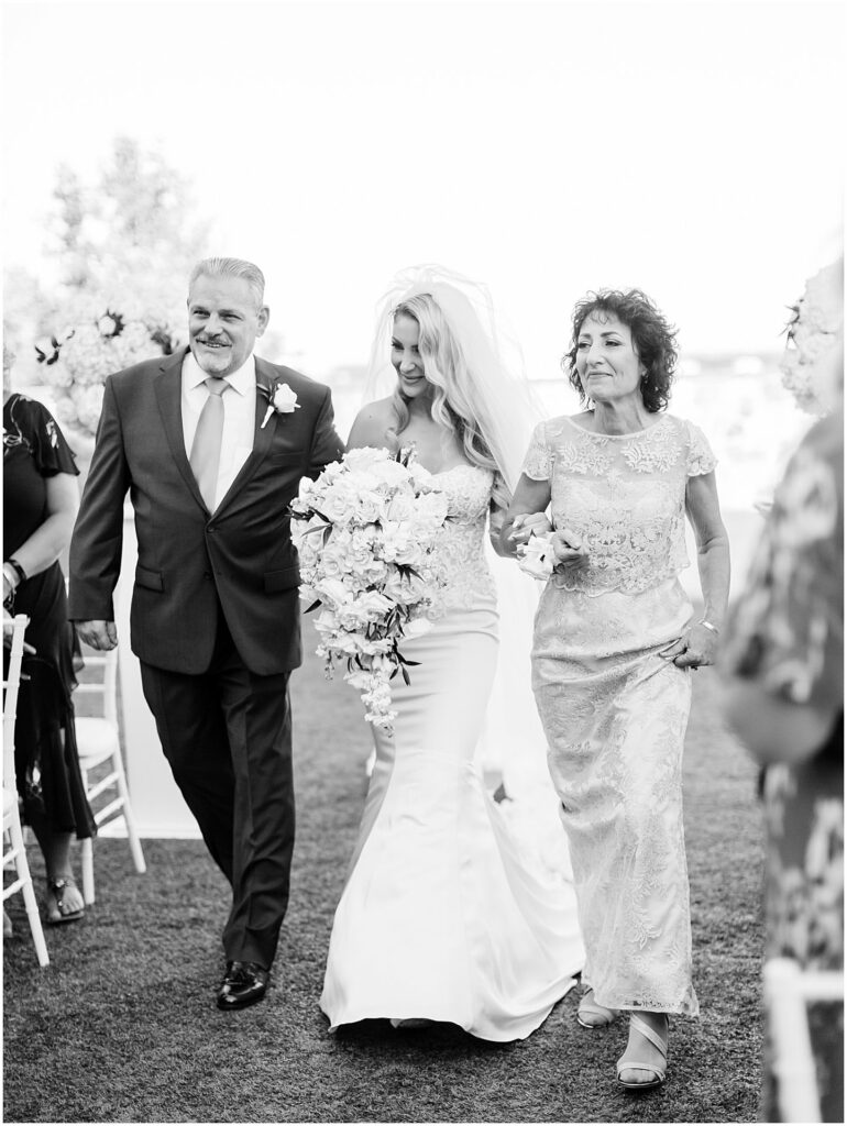 bride walks down aisle with mother of the bride and father of the bride by her side at Bella Collina Orlando Wedding