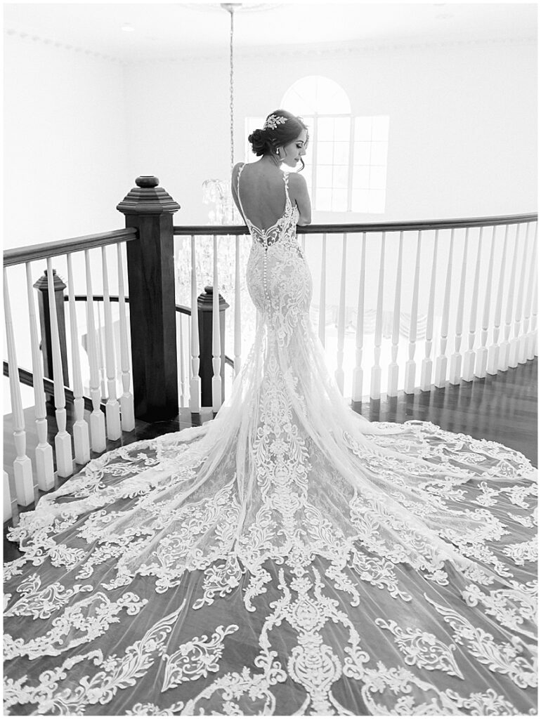 bride stands with back to camera with lace dress and long train behind her at the luxmore grande estate orlando wedding