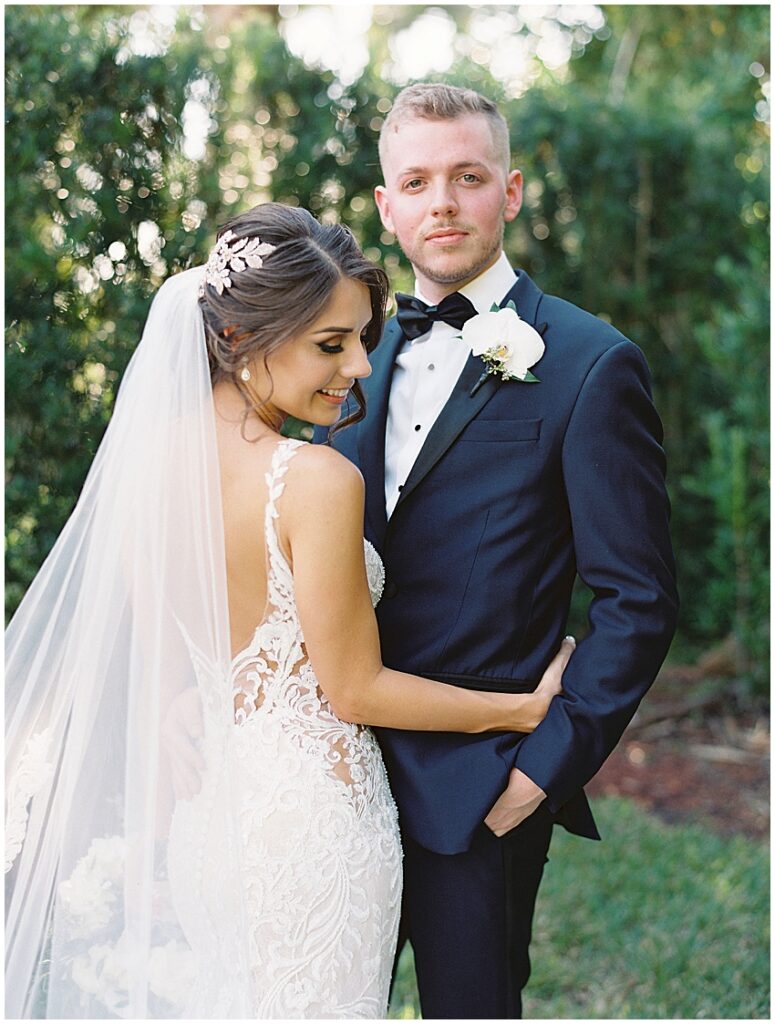 groom looks at camera and smiles while bride holds him close at the luxmore grande estate wedding