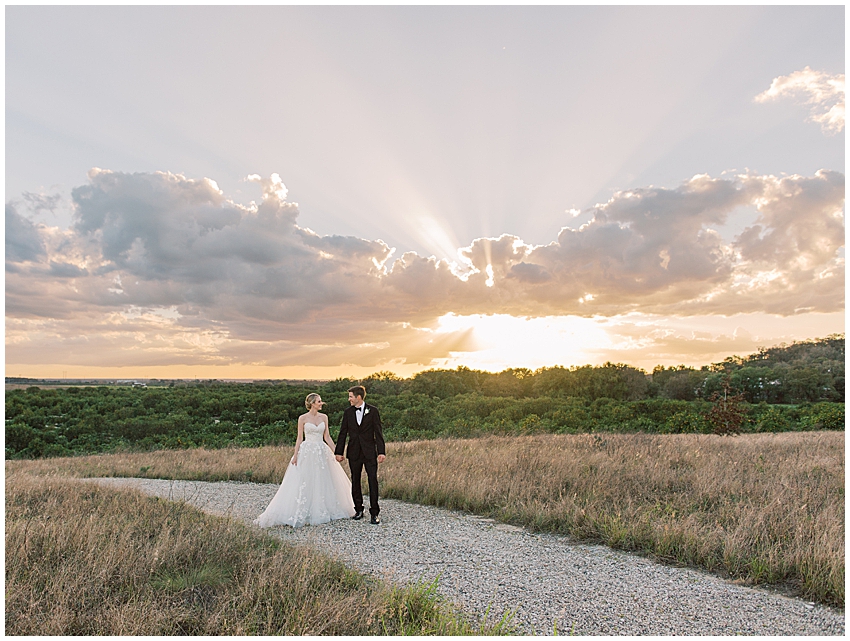 couple walk through grassy field with sunset behind them at Bok Tower gardens wedding
