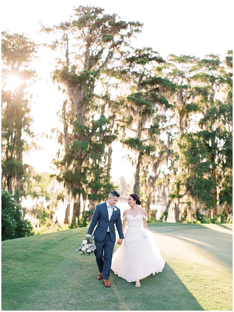 bride and groom walk hand in hand down a hill with golden sunlight behind them at isleworth country club wedding