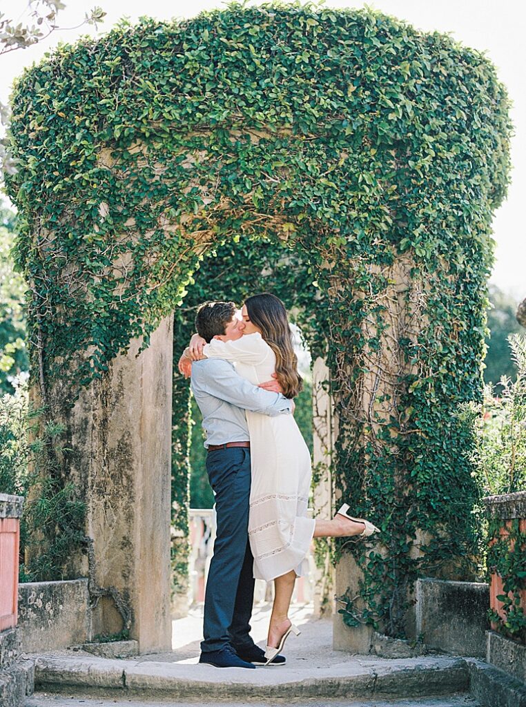 An ivy covered gazebo serves at the backdrop for a couple kissing on medium format film captured by Kt Crabb.